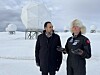 To personer prater foran store hvite radomer i et snødekt landskap.