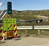 Mobilt trafikkvarsel med grønt lys og skilt ved en vei med bro i bakgrunnen.