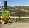 Mobilt trafikkvarsel med grønt lys og skilt ved en vei med bro i bakgrunnen.