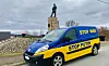 Blå og gul varebil med teksten «STOP WAR» og «STOP PUTIN» parkert foran et monument.