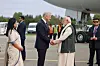 Officials shaking hands on an airport tarmac near a large aircraft with staff and vehicles behind them.