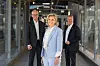 Tre personer står og smiler i en lys glassgang med industriell arkitektur.