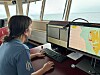 Person seated at a desk using dual monitors with maps inside a room overlooking the water.