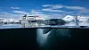 Cruise ship navigating Antarctic waters beside icebergs, shown in a split view with the underwater ice visible.