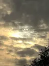 Dramatisk himmel med mørke skyer, gyllent sollys og en delvis formørket sol over trær.