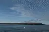 Rolig hav med en lang, lav øyprofil i horisonten under en skyet himmel.