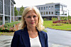 Blond kvinne står foran moderne kontorbygg og et grønt uteområde.