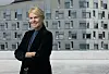 Smilende kvinne i mørke klær foran en moderne bygning.