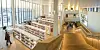 Lyst bibliotek med bokhyller, høye vinduer, mennesker og bred tretrapp.