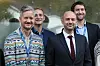 Fire menn med navneskilt står samlet foran en glassvegg.