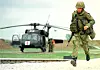 Kamuflert soldat går foran et militærhelikopter med rødt kors.