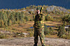 Soldat i feltuniform står på en grusvei foran skog og fjell.