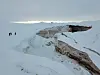 Snødekt brelandskap på Austfonna med issprekker og to små personer i det fjerne.