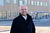 Mann i mørk frakk foran en moderne bygning med store vinduer.