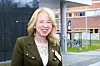 Smilende kvinne i grønn jakke foran en moderne bygning.