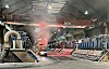 Forklift inside a warehouse with stacked industrial materials and machinery along both sides.
